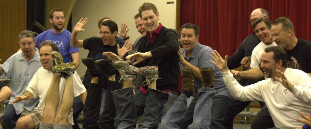 Masters singers cheering around the piano at a rehearsal